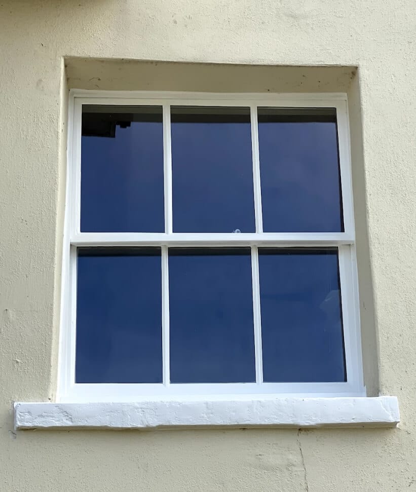 A white sash window with three panes in each sash in a cream rendered wall