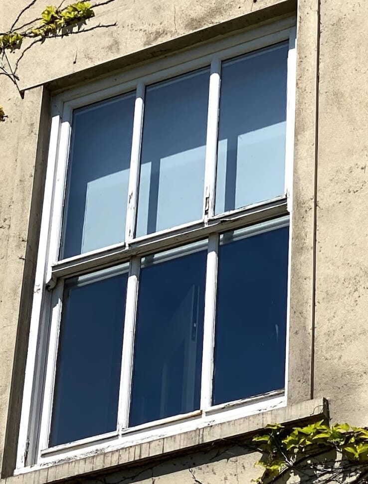 A sash window with three tall panes in each sash in a rendered wall