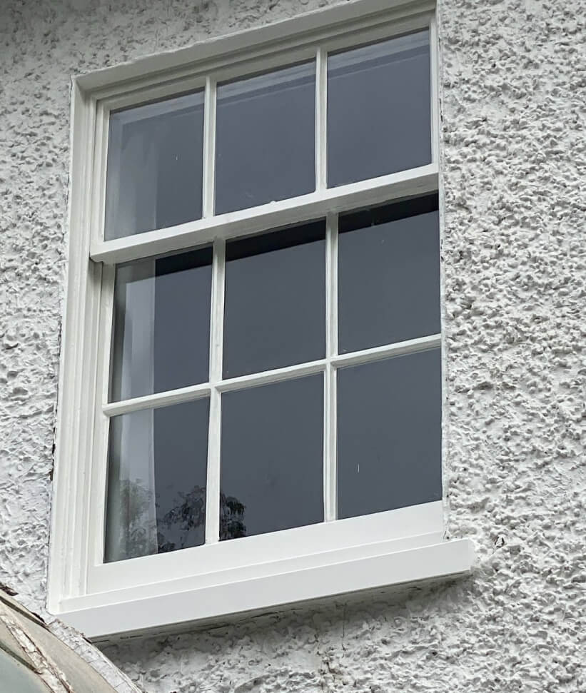 A sash window with three panes in the upper sash and six in the lower, in a rendered wall