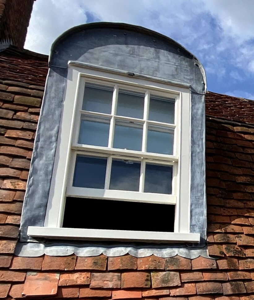 A dormer sash window three panes wide in a lead-clad dormer, with its lower sash open