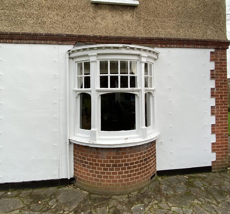 A small bow window with curved half-Georgian sashes on a white rendered wall