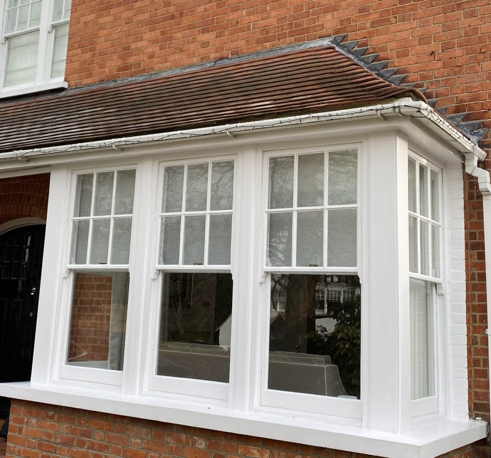 A box bay of half-Georgian sashes under a tiled roof on a red-brick house