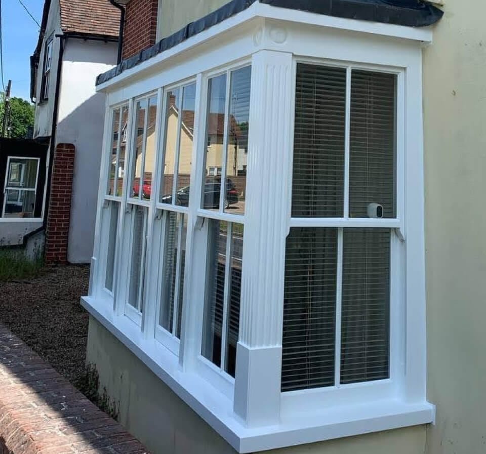 A box bay of centre-bar sash windows on a rendered house, freshly painted white