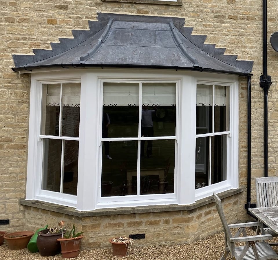A canted bay of three centre-bar sash windows under a lead roof on a stone house