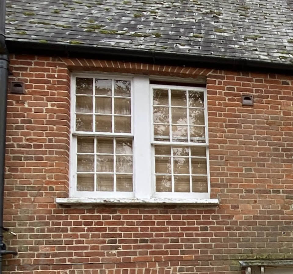 Two Georgian-pattern sashes side by side in one frame in a red-brick wall under a slate roof