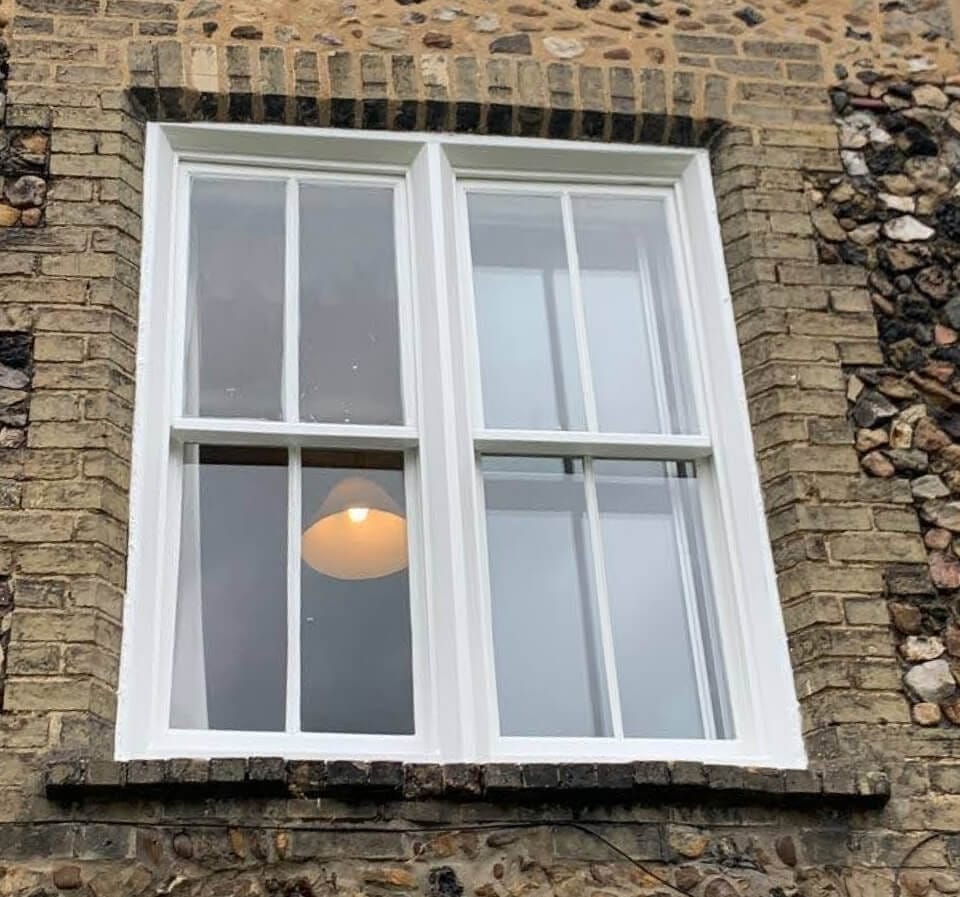 Two centre-bar sashes side by side in one white frame in a flint and brick wall