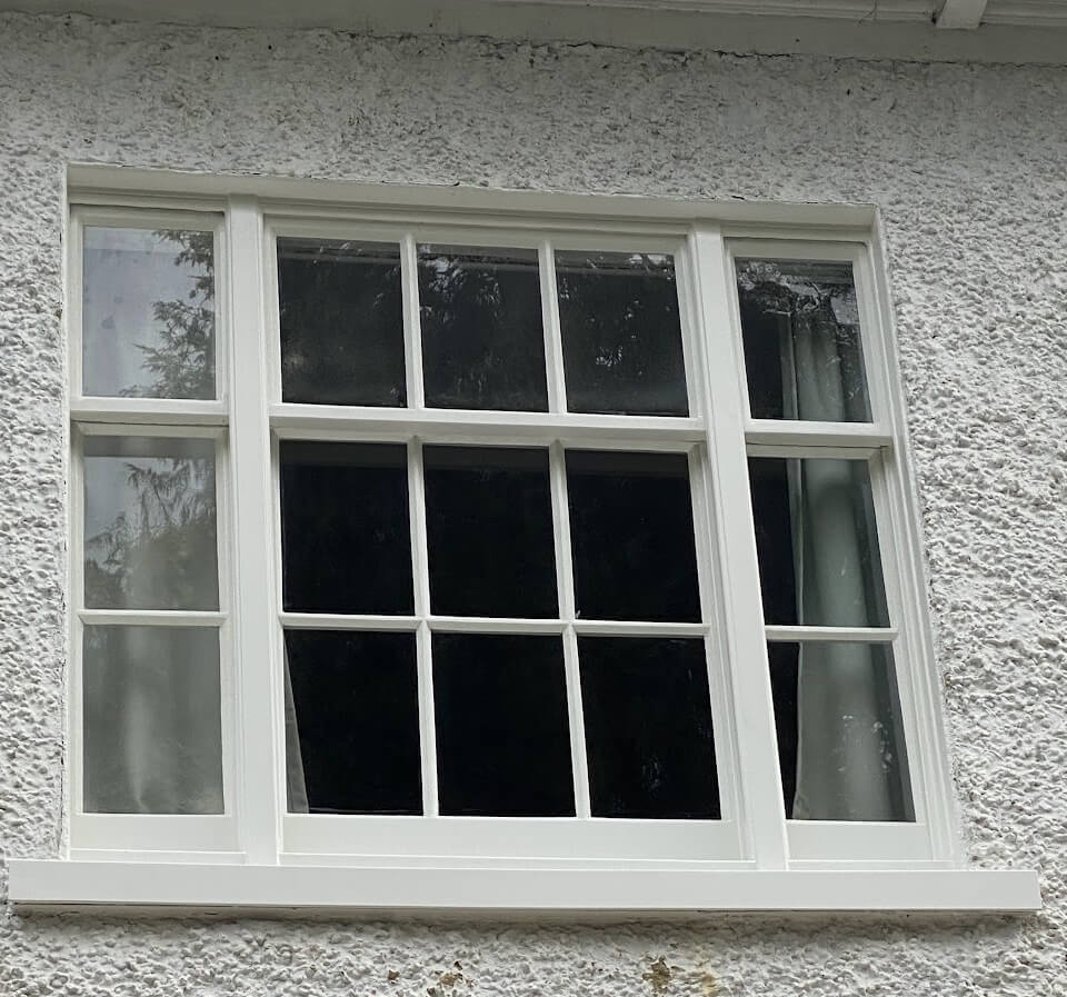 A three-part sash window: a six-over-six centre sash between two narrow sashes in a rendered wall