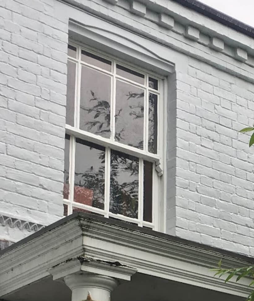 A sash window with a margin border of narrow panes in each sash, above a porch on a white painted brick house