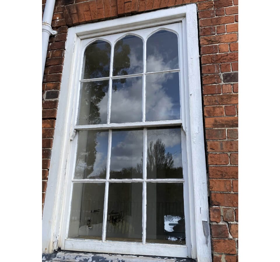 A sash window with pointed tops to the upper panes in a red-brick wall
