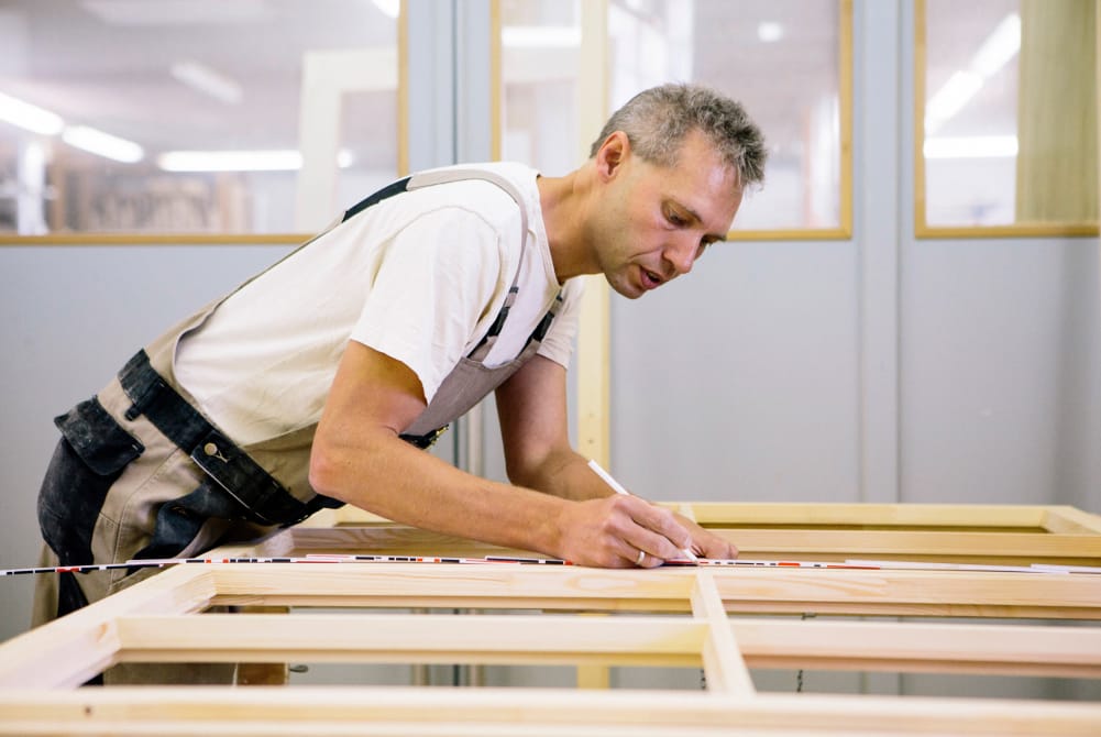 A joiner in a workshop marking out a new timber window frame on a bench