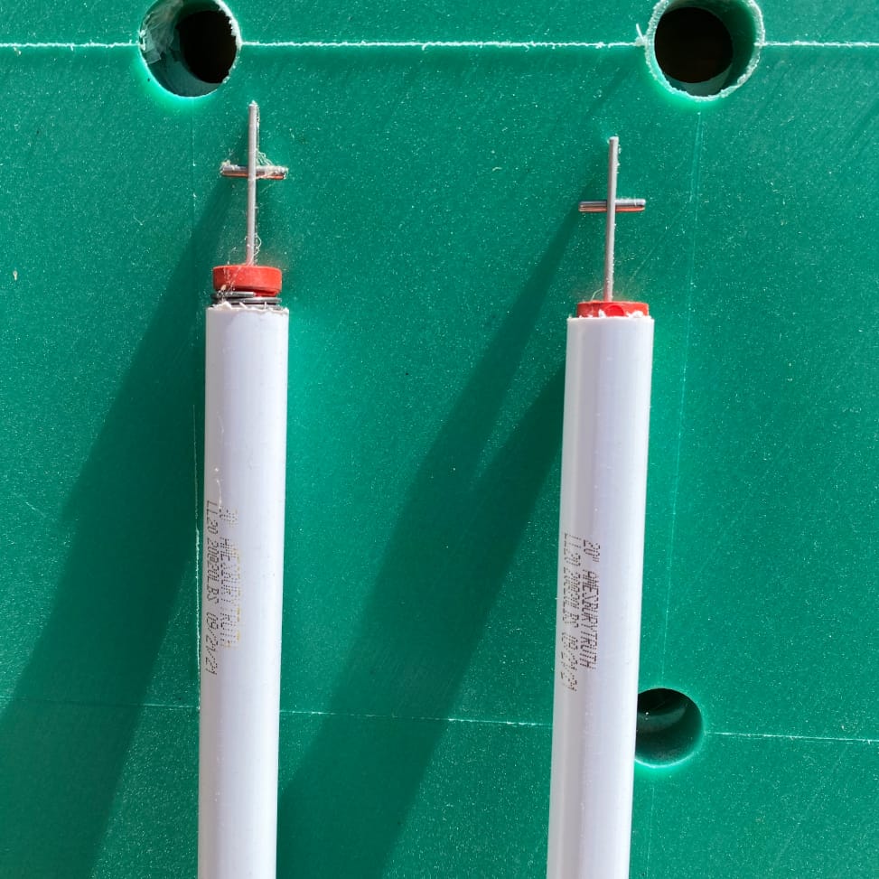 Two white spiral sash balances with red end caps and cross-pin rods, laid side by side on a green board