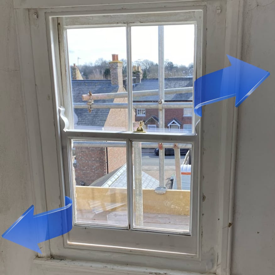 A sash window with the lower section partially raised and blue arrows indicating the window’s opening direction, as seen in many homes needing Sash Windows Repair in Hitchin. Houses and rooftops are visible outside.